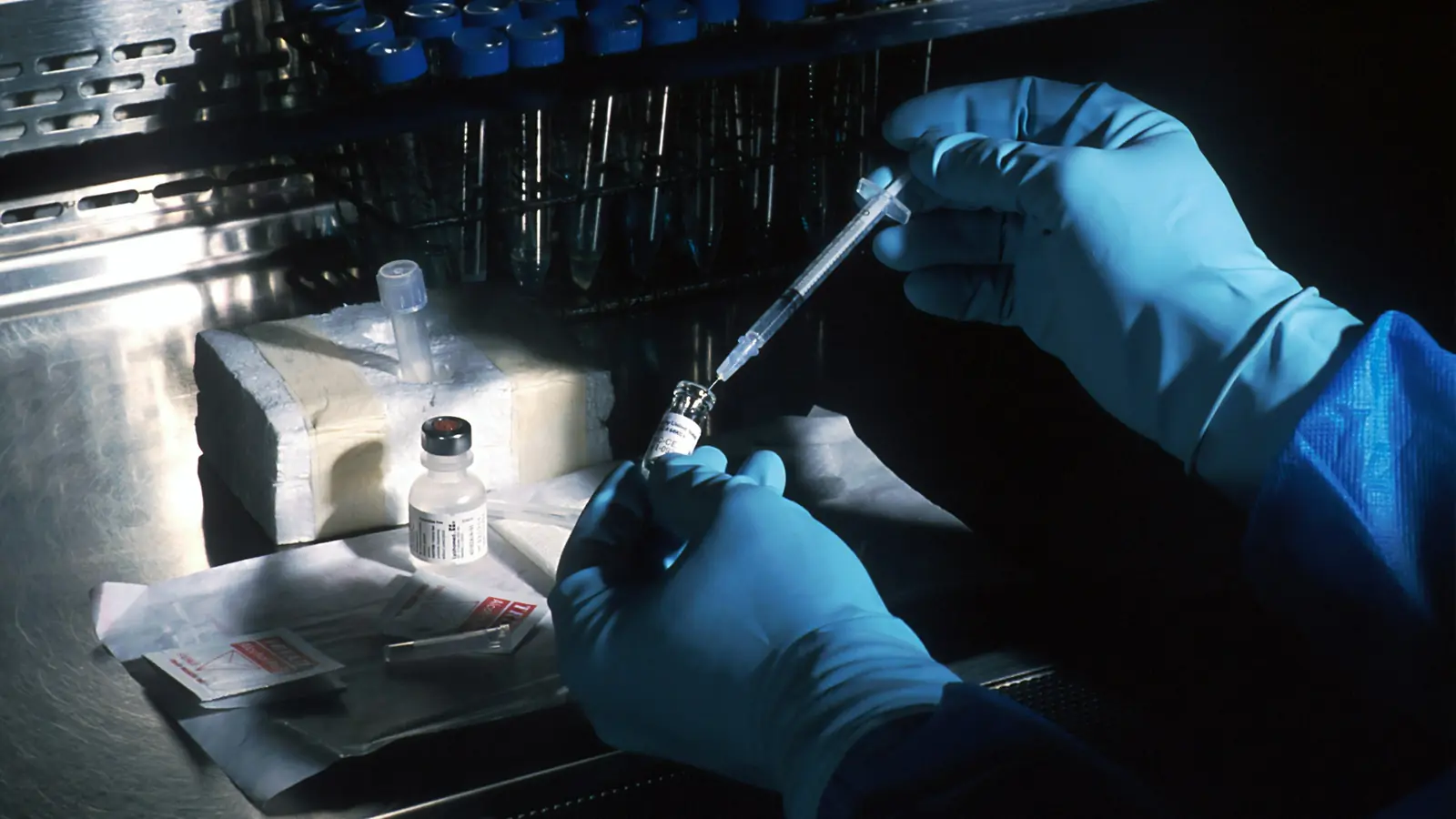 Gloved hands drawing liquid from a vial with a syringe